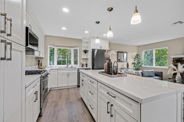 kitchen featuring decorative light fixtures, white cabinetry, a center island, light stone counters, and stainless steel appliances