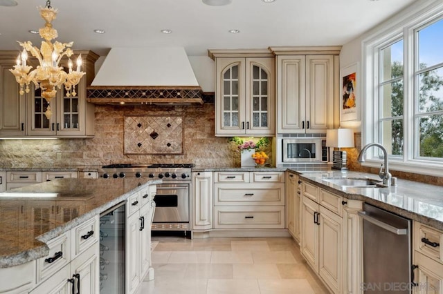 kitchen with appliances with stainless steel finishes, sink, hanging light fixtures, cream cabinets, and custom range hood