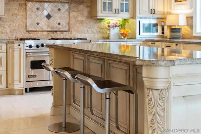 kitchen featuring light stone counters, stainless steel appliances, decorative backsplash, and cream cabinetry