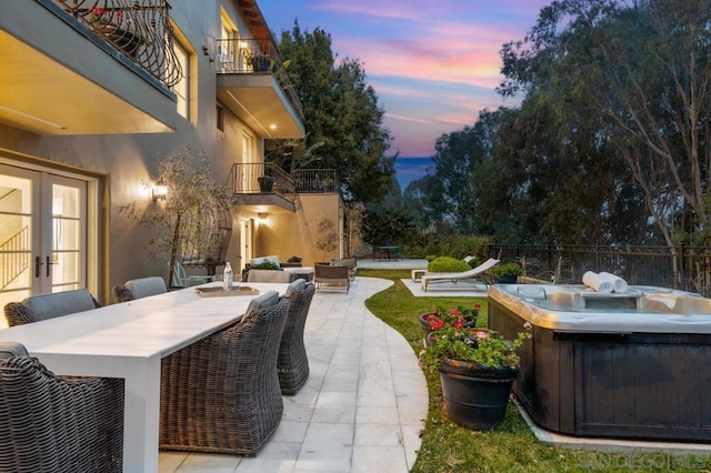 patio terrace at dusk featuring a hot tub and a balcony