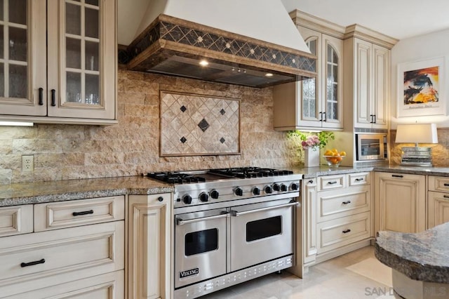 kitchen with stone counters, decorative backsplash, custom exhaust hood, stainless steel appliances, and cream cabinetry