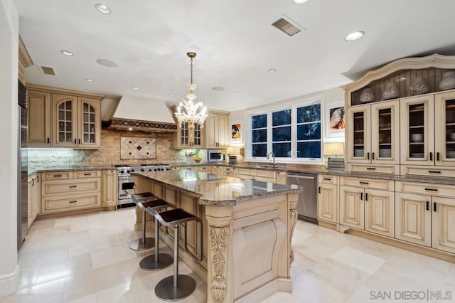 kitchen featuring a kitchen island, appliances with stainless steel finishes, a kitchen bar, custom exhaust hood, and hanging light fixtures