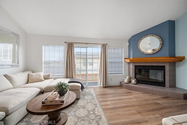 living room with a tile fireplace, vaulted ceiling, and hardwood / wood-style floors