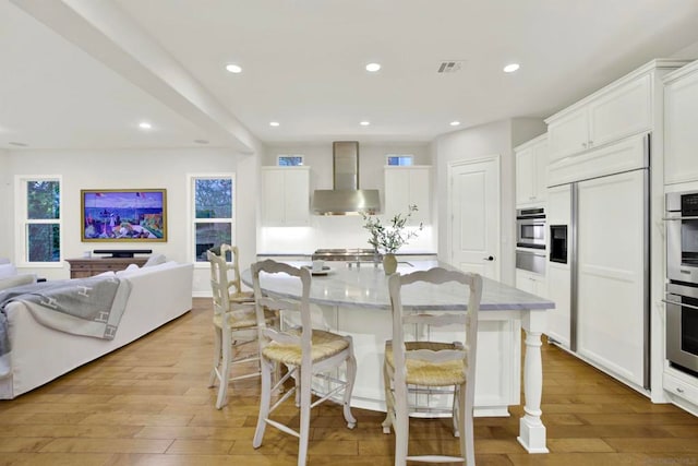 kitchen featuring a large island with sink, white cabinetry, a breakfast bar, and wall chimney exhaust hood