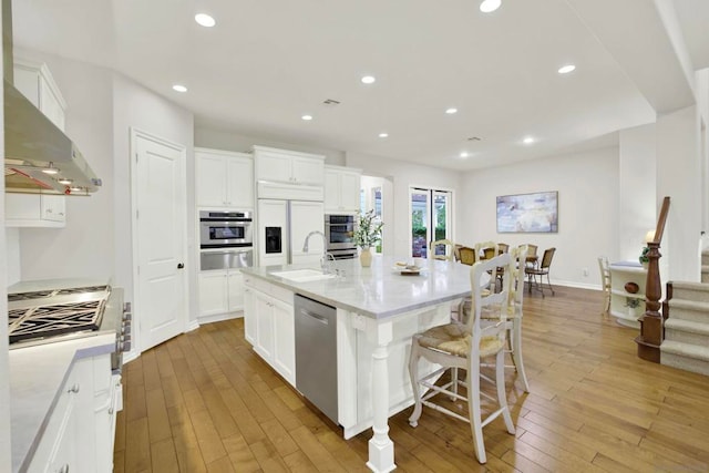 kitchen with sink, a center island with sink, light wood-type flooring, appliances with stainless steel finishes, and white cabinets