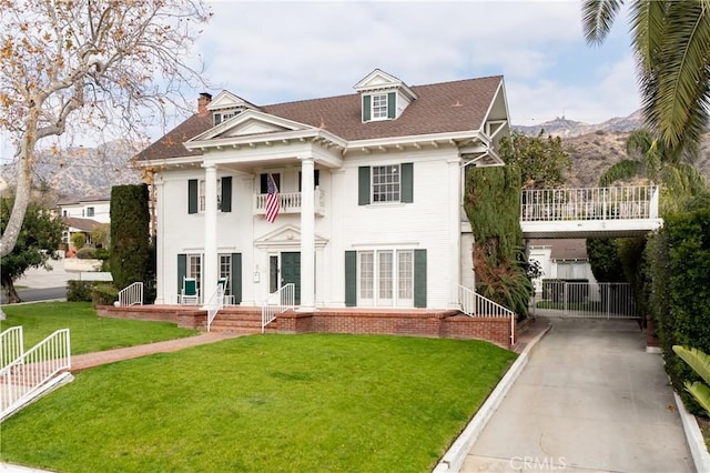 greek revival house featuring a mountain view, a front lawn, and a balcony