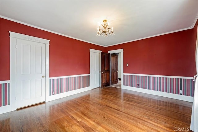 unfurnished room featuring an inviting chandelier, ornamental molding, and hardwood / wood-style floors