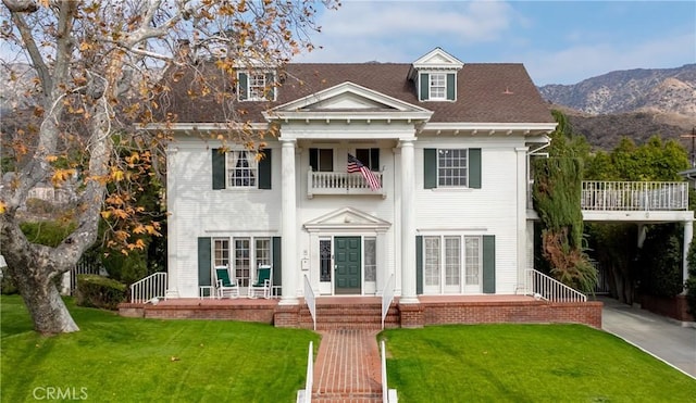 view of front facade featuring a mountain view, a front yard, and a balcony