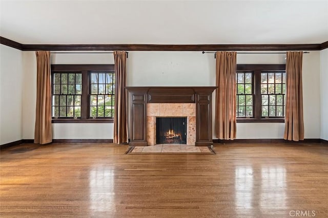 unfurnished living room with ornamental molding, plenty of natural light, a tiled fireplace, and light hardwood / wood-style flooring