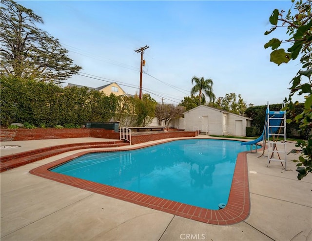 view of pool featuring a water slide, a patio area, and a storage unit