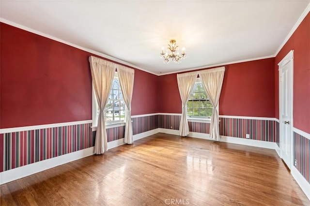 empty room with wood-type flooring, ornamental molding, and a chandelier