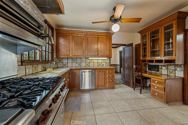 kitchen with sink, tasteful backsplash, built in desk, light tile patterned floors, and appliances with stainless steel finishes