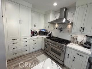 kitchen with wall chimney range hood, light hardwood / wood-style flooring, stainless steel appliances, and white cabinets