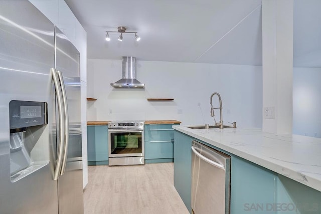 kitchen featuring sink, light stone counters, light wood-type flooring, stainless steel appliances, and wall chimney range hood