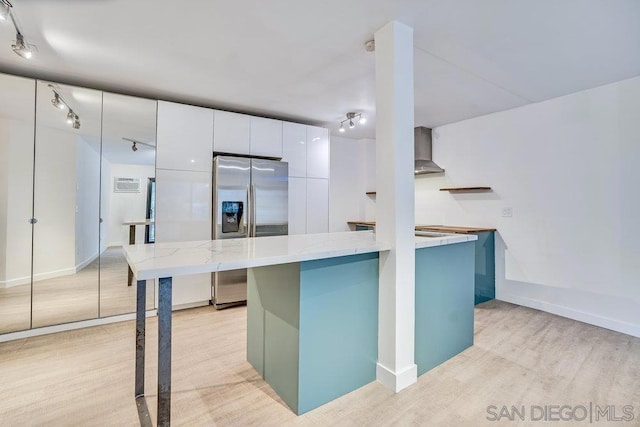 kitchen featuring white cabinetry, a center island, stainless steel fridge, light hardwood / wood-style floors, and wall chimney range hood