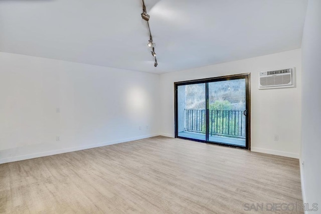 empty room featuring track lighting, a wall mounted AC, and light wood-type flooring