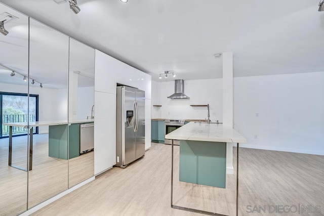 kitchen with green cabinetry, light wood-type flooring, appliances with stainless steel finishes, white cabinets, and wall chimney range hood