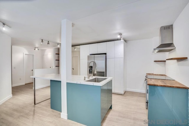 kitchen featuring sink, white cabinets, stainless steel refrigerator with ice dispenser, light wood-type flooring, and wall chimney exhaust hood