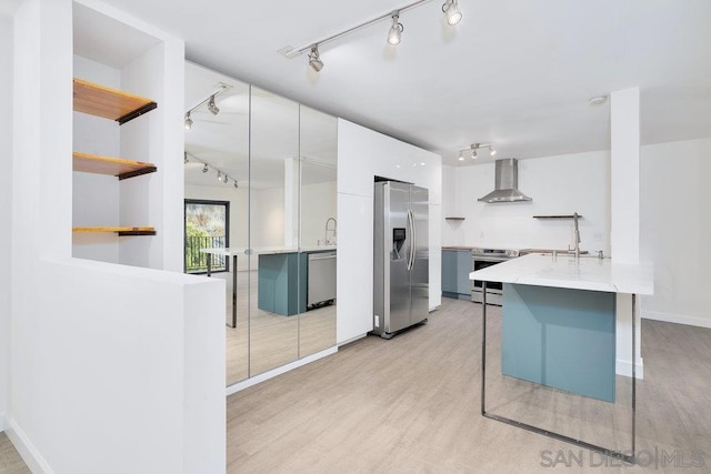 kitchen with a breakfast bar, white cabinets, wall chimney exhaust hood, stainless steel appliances, and light hardwood / wood-style flooring