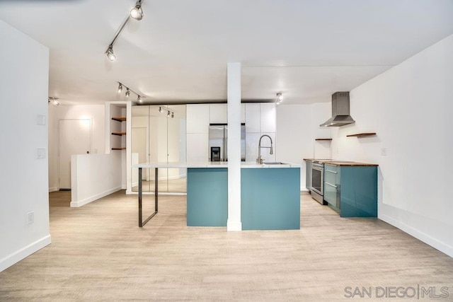 kitchen with sink, appliances with stainless steel finishes, white cabinets, a center island with sink, and wall chimney exhaust hood