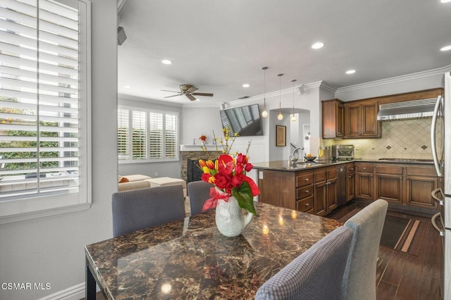 dining space with a stone fireplace, sink, ornamental molding, dark hardwood / wood-style flooring, and ceiling fan