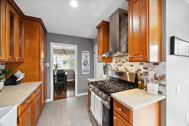 kitchen featuring tasteful backsplash, wall chimney exhaust hood, light stone counters, and stainless steel gas stove