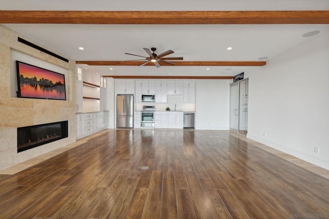 unfurnished living room featuring sink, dark wood-type flooring, a fireplace, and beamed ceiling