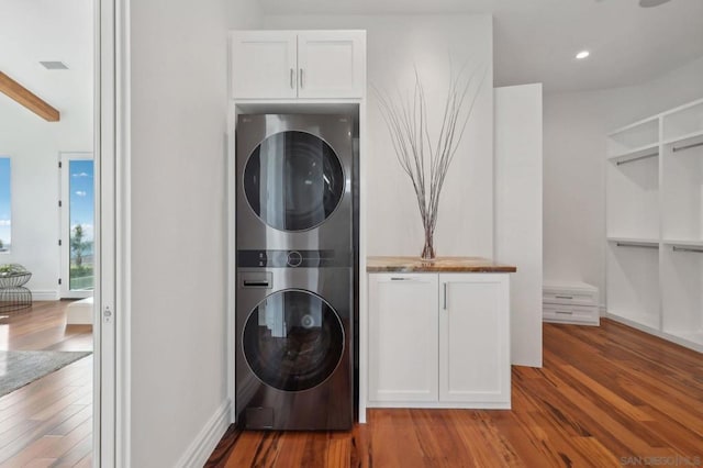 laundry room featuring cabinets, wood-type flooring, and stacked washer and clothes dryer