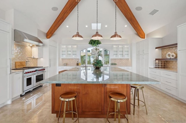 kitchen with a large island, white cabinets, decorative light fixtures, wall chimney exhaust hood, and range with two ovens