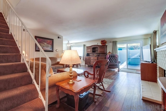 living room with dark wood-type flooring, ceiling fan, and a brick fireplace