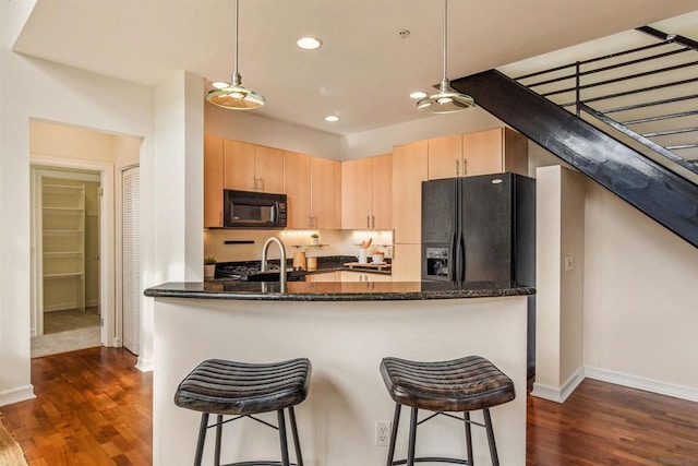 kitchen with sink, decorative light fixtures, light brown cabinets, dark stone counters, and black appliances