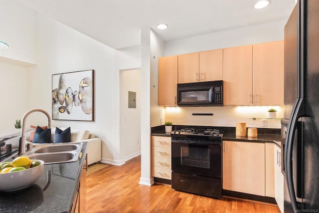 kitchen with sink, black appliances, light hardwood / wood-style floors, light brown cabinetry, and dark stone counters