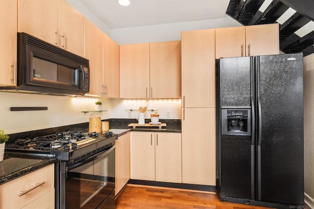 kitchen featuring light wood-type flooring, dark stone countertops, light brown cabinetry, and black appliances