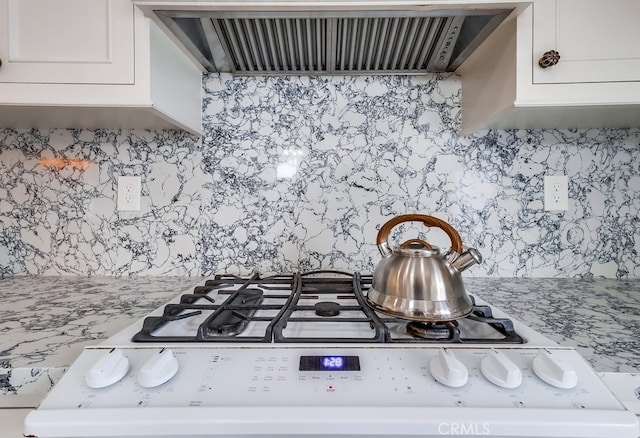 details with white gas stove, white cabinetry, light stone counters, decorative backsplash, and exhaust hood