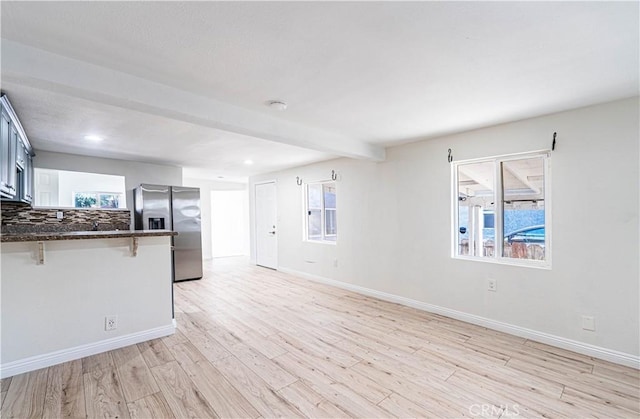 interior space featuring baseboards, light wood finished floors, beamed ceiling, and a healthy amount of sunlight