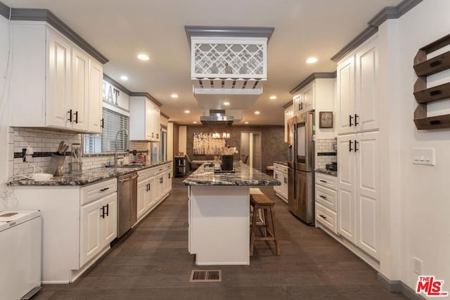 kitchen featuring a kitchen island, appliances with stainless steel finishes, a breakfast bar area, white cabinets, and dark stone counters