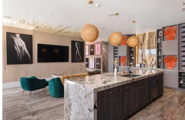 kitchen with pendant lighting, sink, dark brown cabinets, a spacious island, and light stone counters