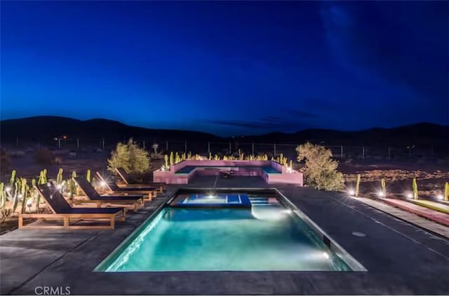 pool at twilight with an in ground hot tub, a mountain view, and a patio