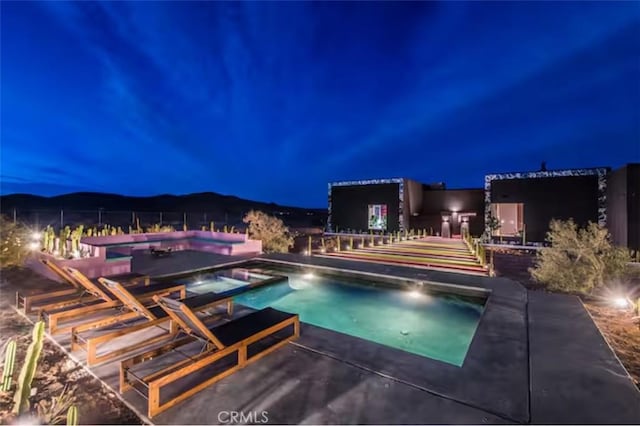 pool at night featuring a mountain view and a patio area