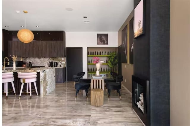 kitchen with a breakfast bar, decorative light fixtures, decorative backsplash, light stone counters, and dark brown cabinets