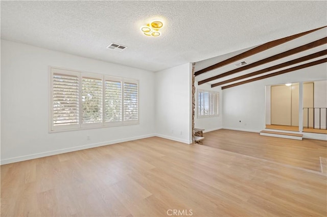 empty room featuring vaulted ceiling with beams, light hardwood / wood-style floors, and a textured ceiling