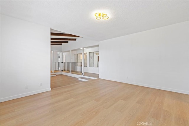 empty room featuring beamed ceiling, a textured ceiling, and light wood-type flooring