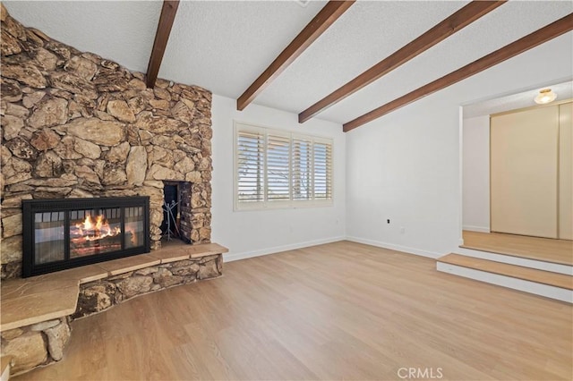 unfurnished living room featuring a stone fireplace, light wood-type flooring, a textured ceiling, and vaulted ceiling with beams