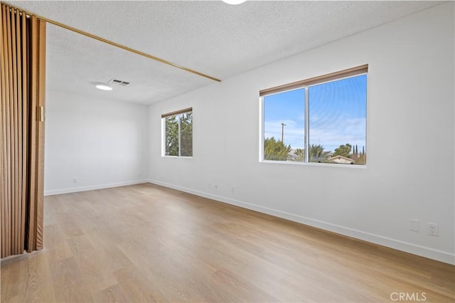 unfurnished room with a textured ceiling and light wood-type flooring