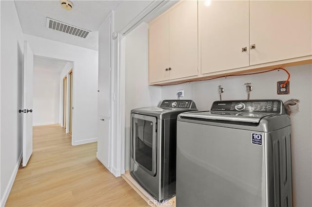 clothes washing area with cabinets, washing machine and clothes dryer, and light hardwood / wood-style flooring