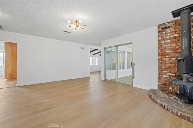 unfurnished living room featuring an inviting chandelier, light wood-type flooring, a textured ceiling, and a wood stove