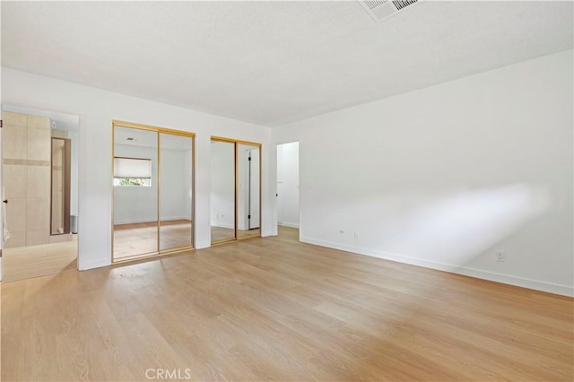 unfurnished bedroom with light wood-type flooring and two closets