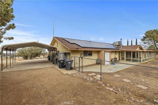 back of property featuring a carport, a sunroom, cooling unit, and solar panels