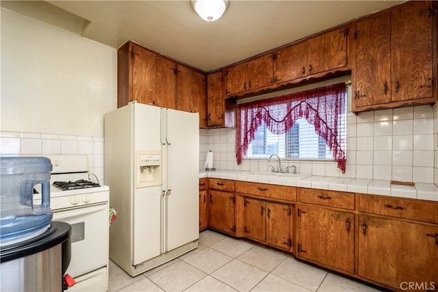 kitchen with tasteful backsplash, sink, light tile patterned floors, tile counters, and white appliances