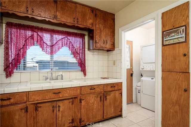 kitchen featuring light tile patterned flooring, stacked washer and clothes dryer, sink, tile countertops, and decorative backsplash